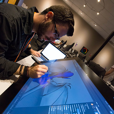 A man in a black shirt draws on a large digital tablet with a stylus.