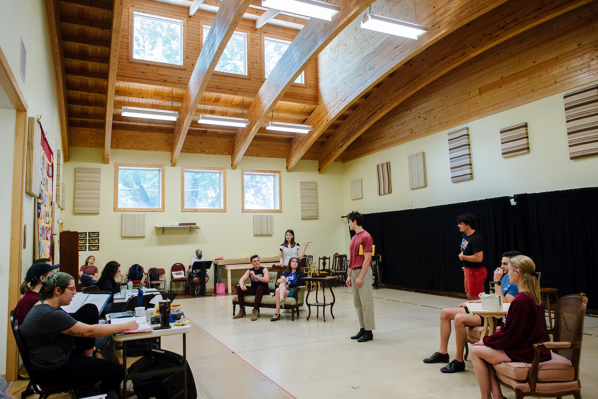 In a large open room with windows, multiple students rehearse in front of faculty members. 
