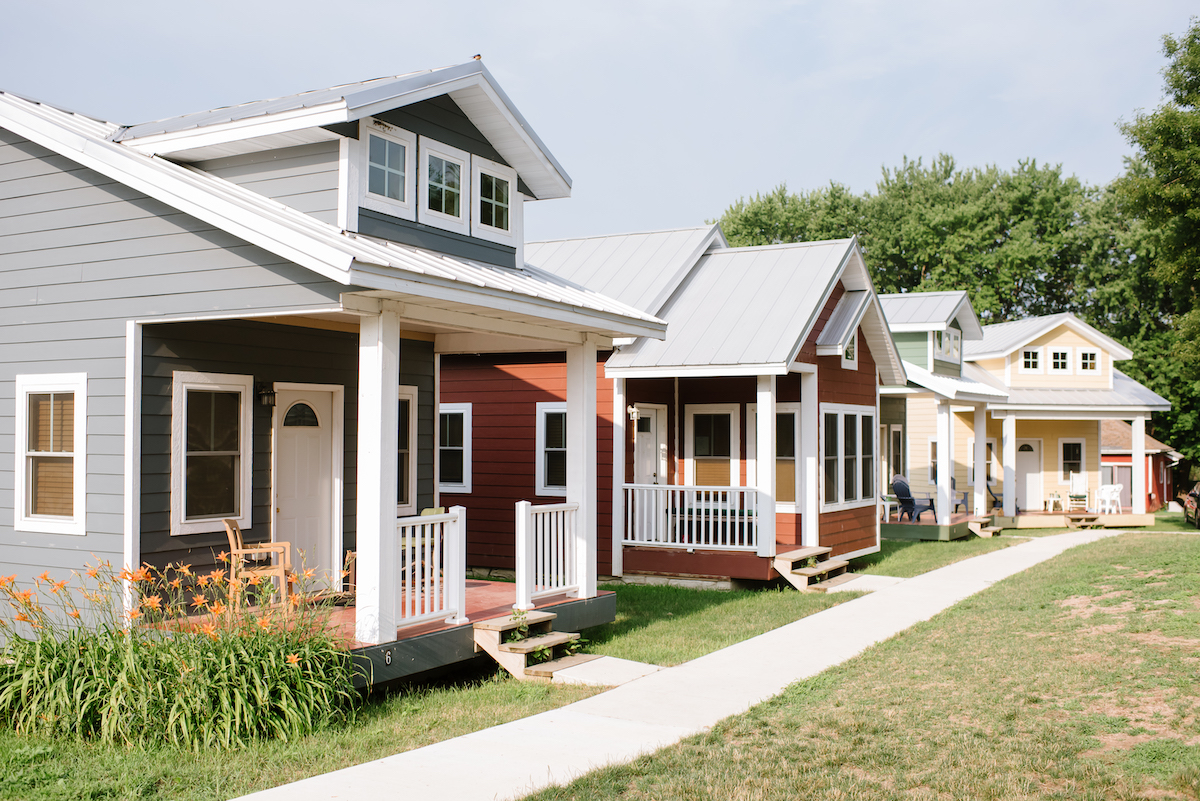 Four modern-looking cottages sit in a row along a walking path on a bright, clear day.