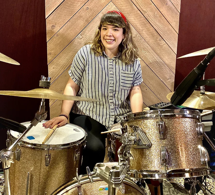 Woman smiling sitting behind gold drum kit