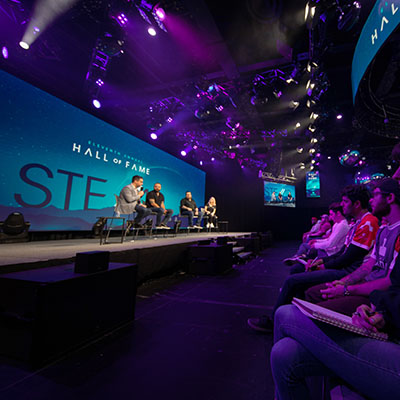 Image of Full Sail indoor stage with 4 Hall of Fame panel and students watching in front row