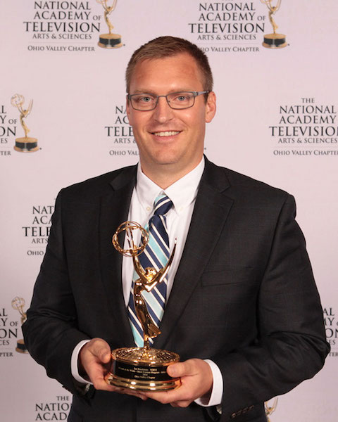 Headshot of Joe Brackman holding an Emmy Award in front of The National Academy of  Television Arts and Sciences Ohio Valley Chapter backdrop