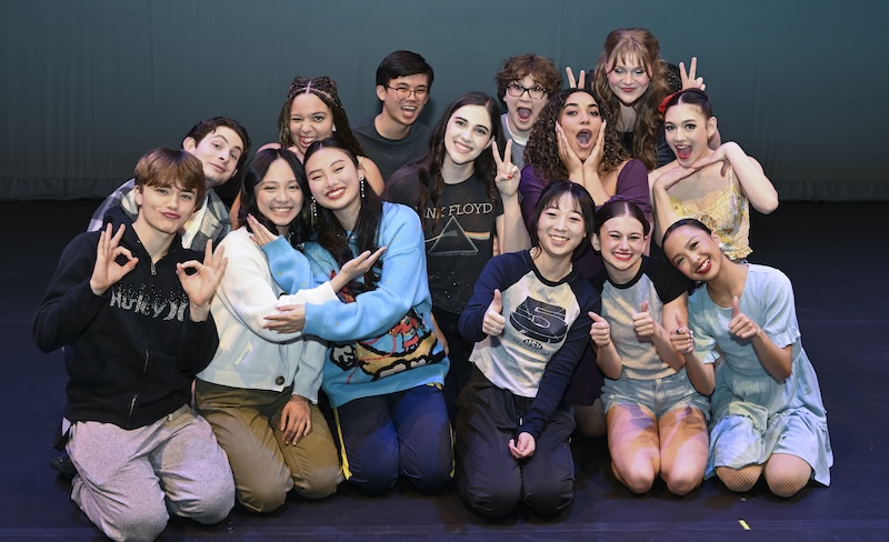 A group of 14 high schoolers pose happily together making various happy hand gestures