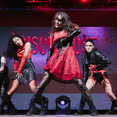 Three students in red and black dance outfits perform a dance on stage
