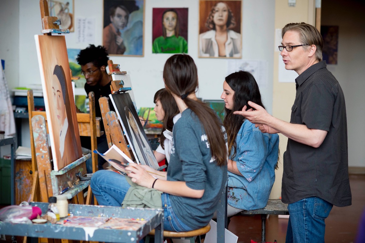 An instructor teaches a group of students who sit at easels painting portraits